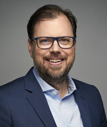 Man med glasögon i ljusblå skjorta och mörkblå kavaj
