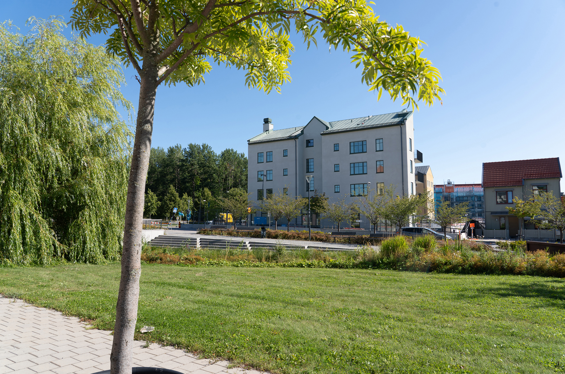 Ett vitt flerbostadshus med en gräsmatta och träd i förgrunden.