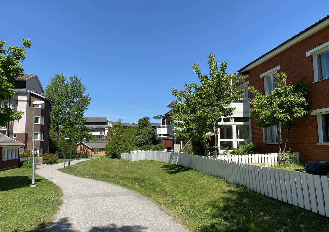 Asfalterad gångväg mellan flerbostadshus i brunt och tvåvånings flerbostadshus i tegel med vita balkonger.