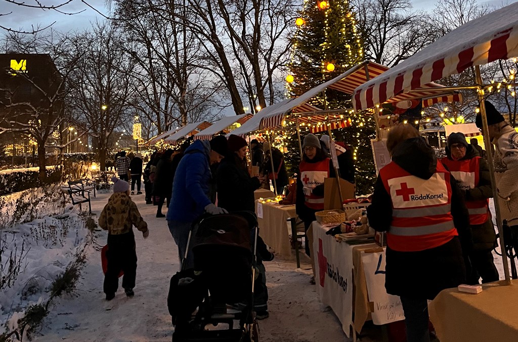 Marknadsstånd och människor i vinterväder med en julgran i bakgrunden.