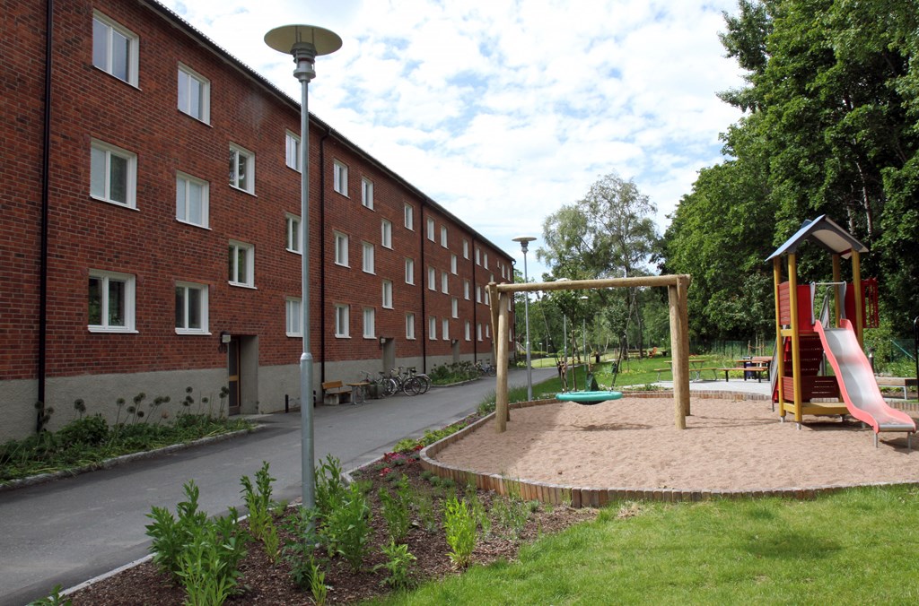 Trevånings flerbostadshus i tegel med en lekpark.