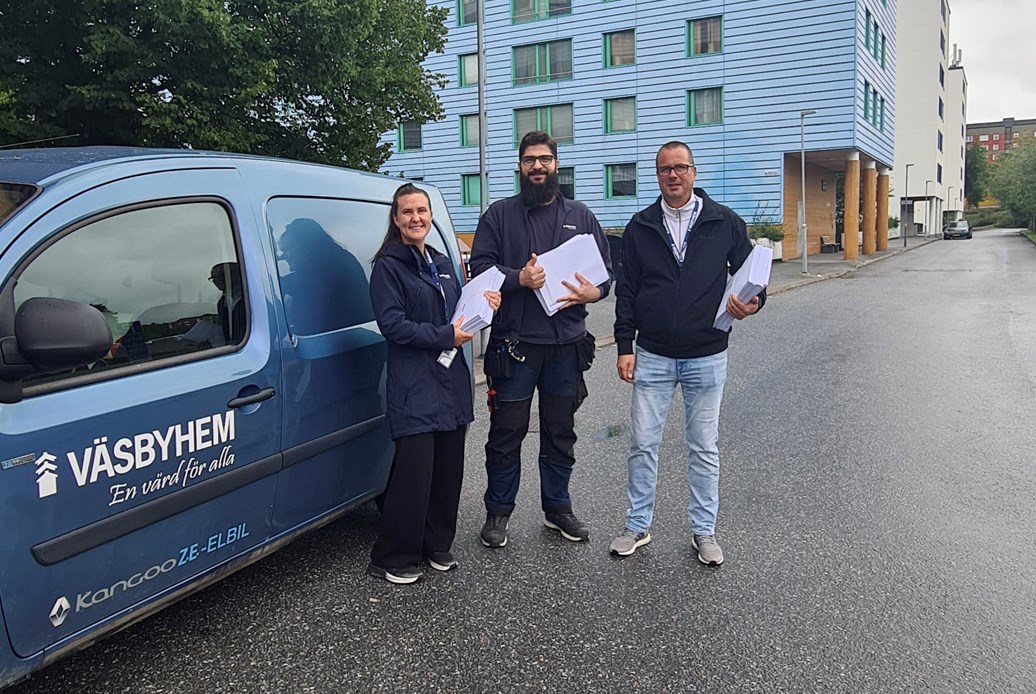 Tre personer invid en Väsbyhemprofilerad bil i ett bostadsområde.