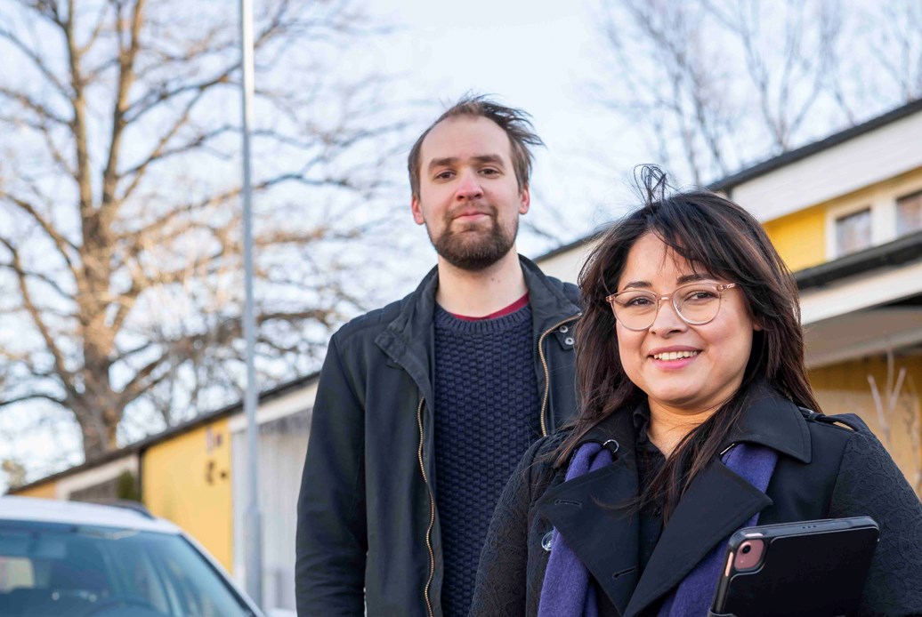 En man och en kvinna som står bredvid en bil med gula radhus i bakgrunden