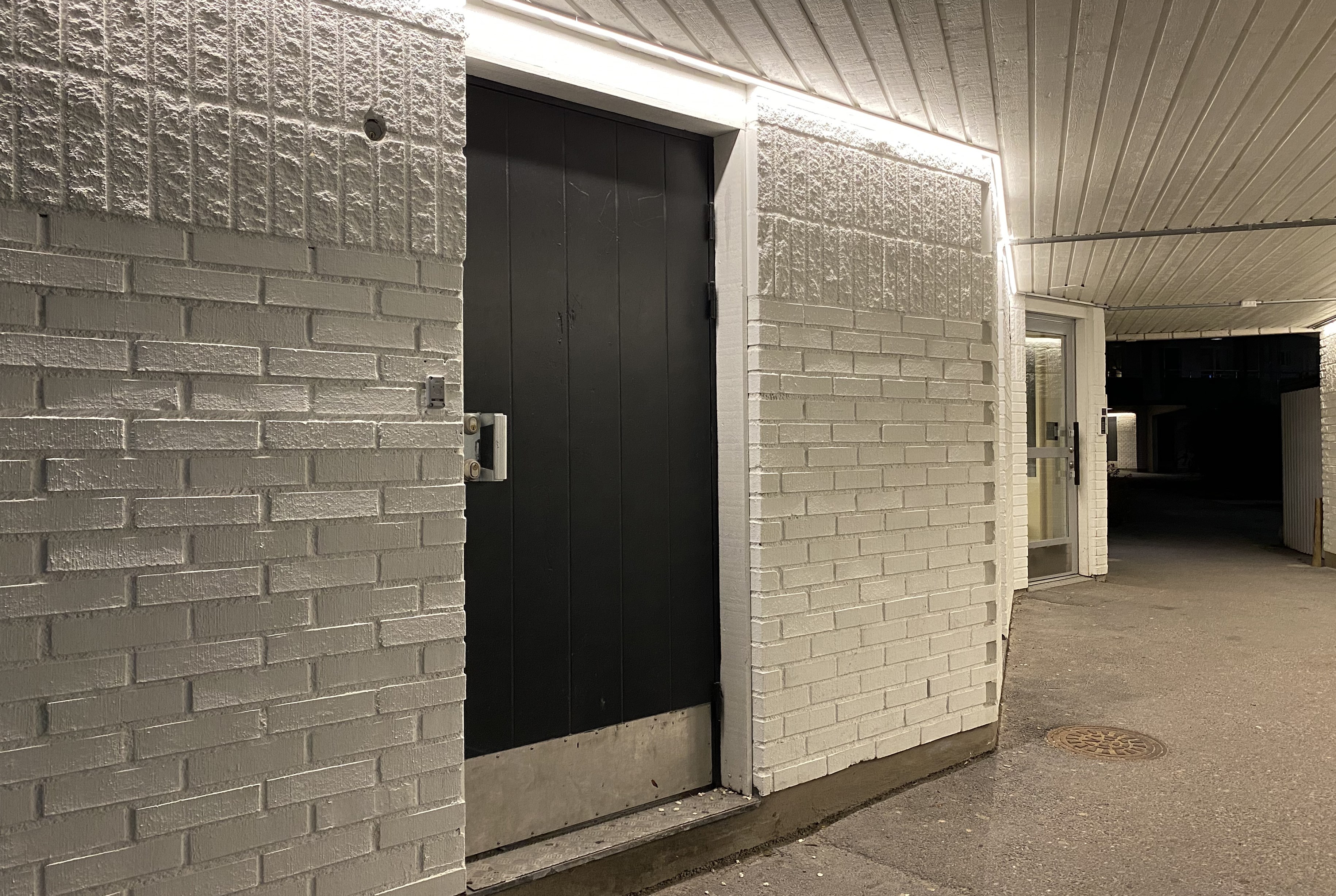Portal i flerbostadshus med vitt tegel och brun dörr.