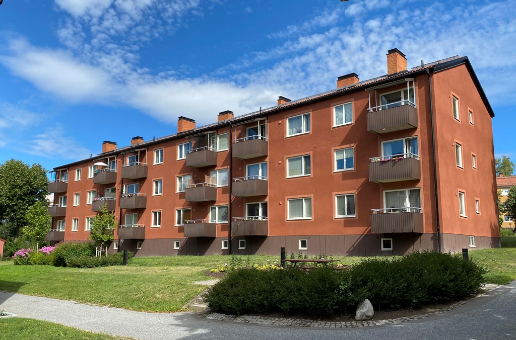 Brunfärgat trevånings flerbostadsshus med bruna balkonger med en gräsmatta och en gångväg i förgrunden