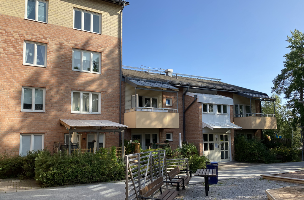 Flerbostadshus i gult och ljusbrunt tegel med bord och bänkar i förgrunden