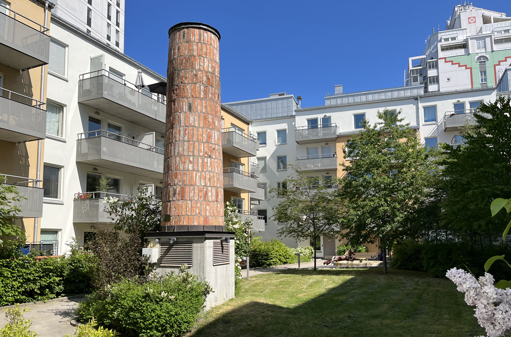 Innergården vid ett flerbostadshus i vitt och gult med en murad skorsten på gården.