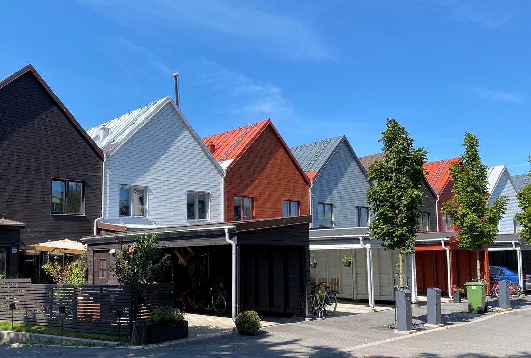 Radhus i färgerna svart, vitt, rött och grått med carportar och träd i förgrunden