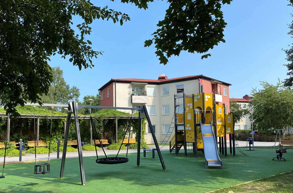 Lekplats framför ett flerbostadshus i tre våningar.