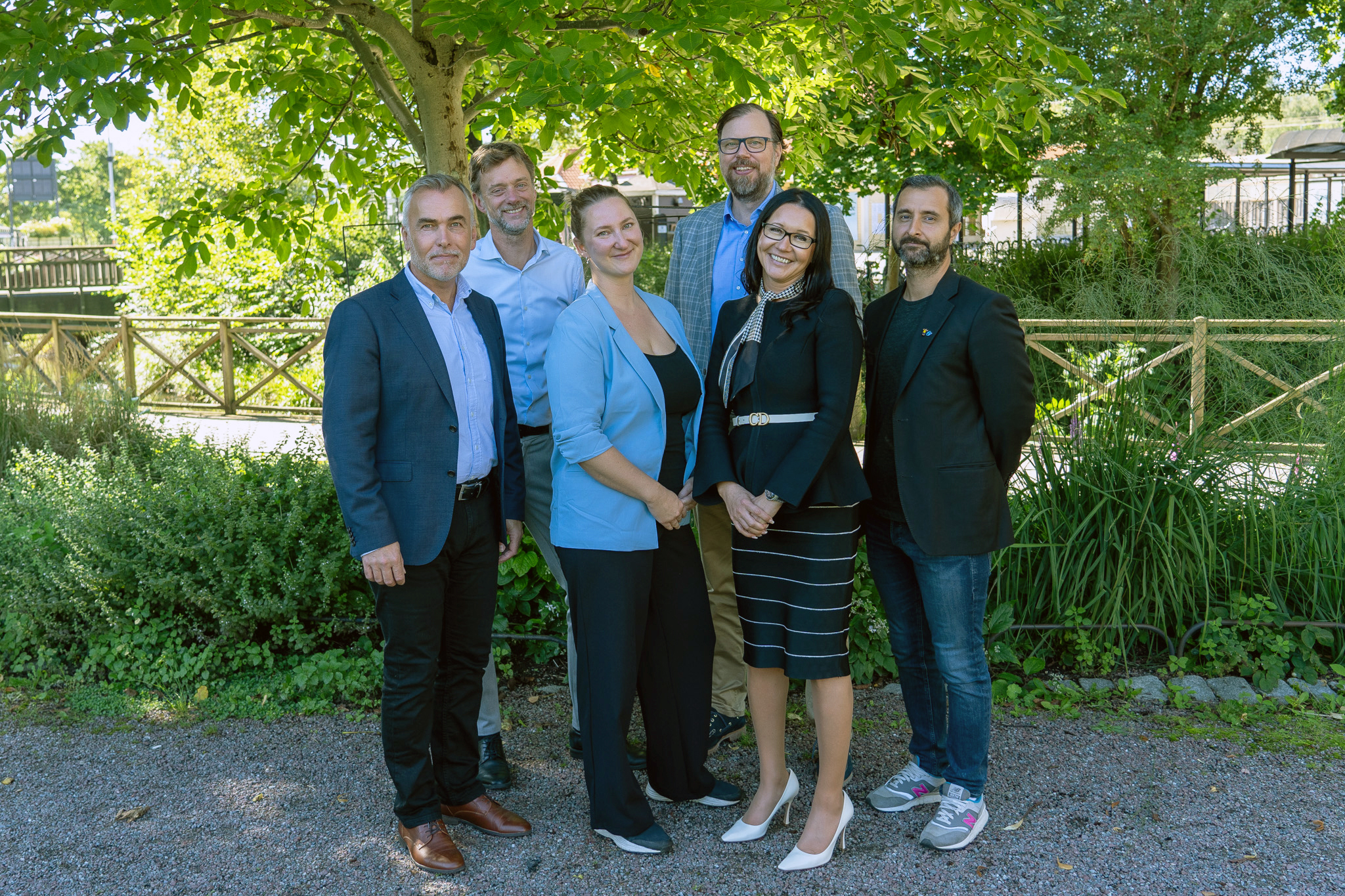 Två kvinnor och fyra män stående i grupp i en parkmiljö.