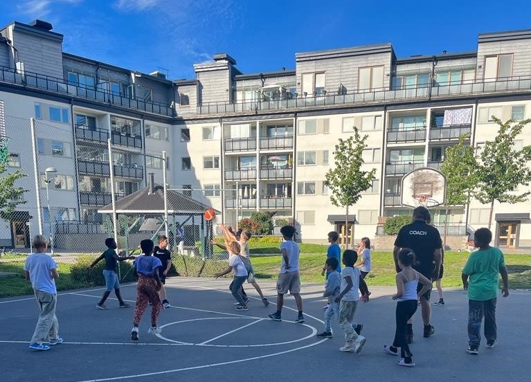 Barn som spelar basket framför ett flerbostadshus.