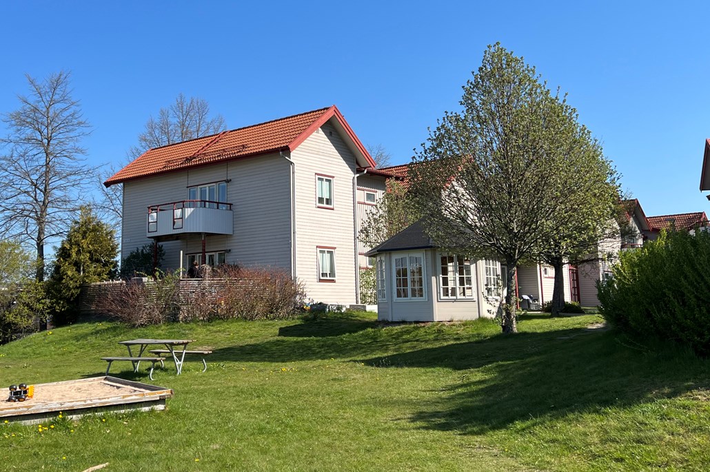 Tvåvånings flerbostadshus i grått och vitt, en sandlåda, gräsmatta och lusthus intill.