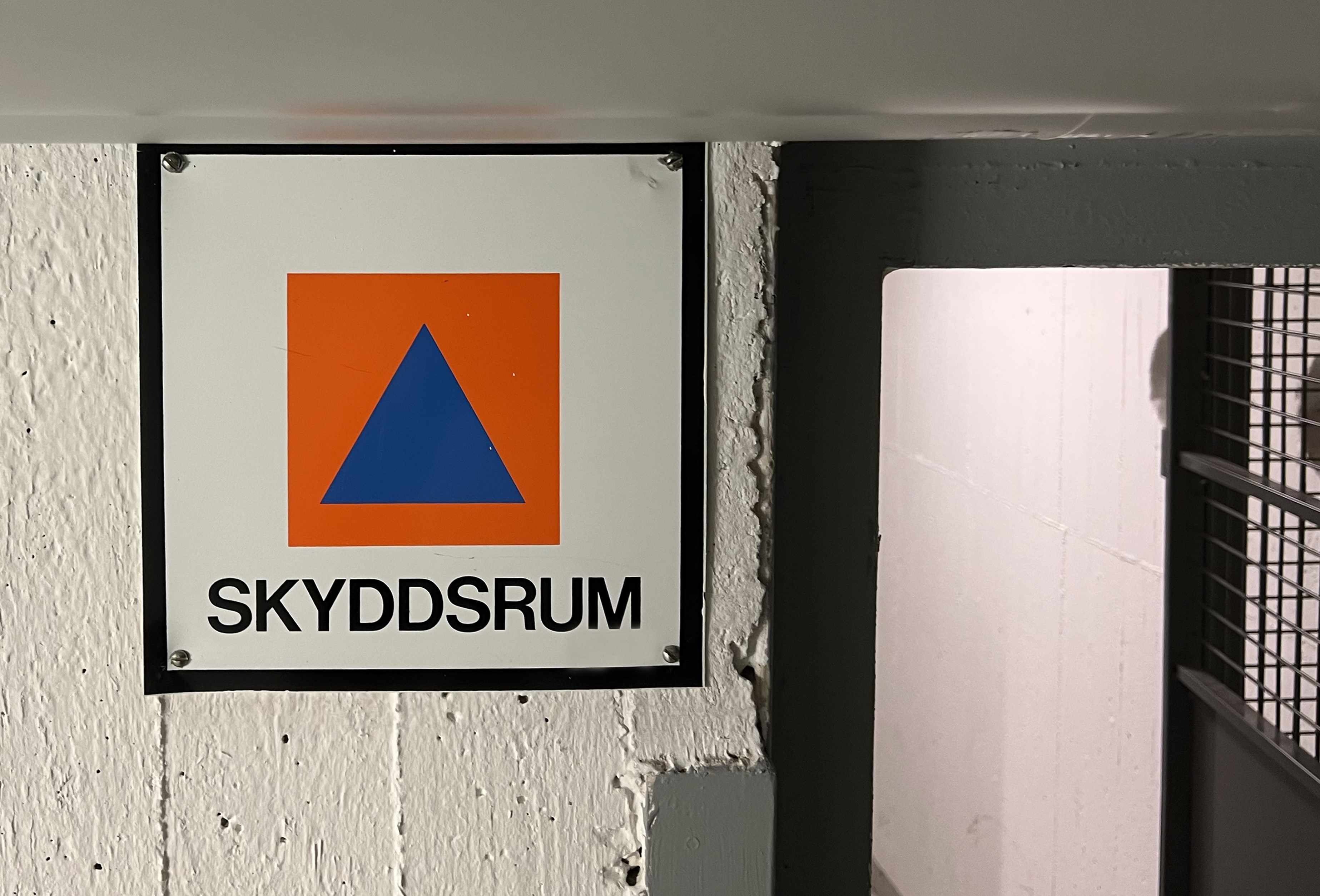 Skylt med ordet skyddsrum under en orange kvadrat med en blå triangel.