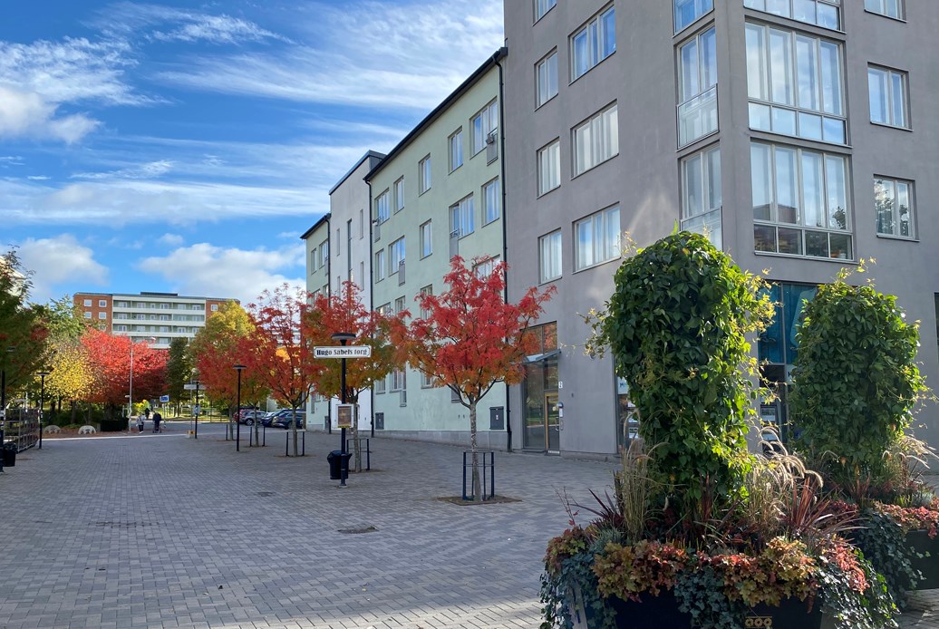 Ljusgrönt och grått flerbostadshus i fem våningar invid ett torg.