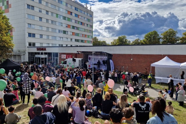 Människor framför scenen utomhus med byggnad i bakgrunden.