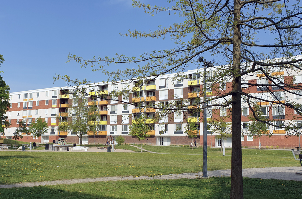 Flerbostadshus i vitt, brunt, orange och gult med stor gräsmatta och en lekpark i förgrunden