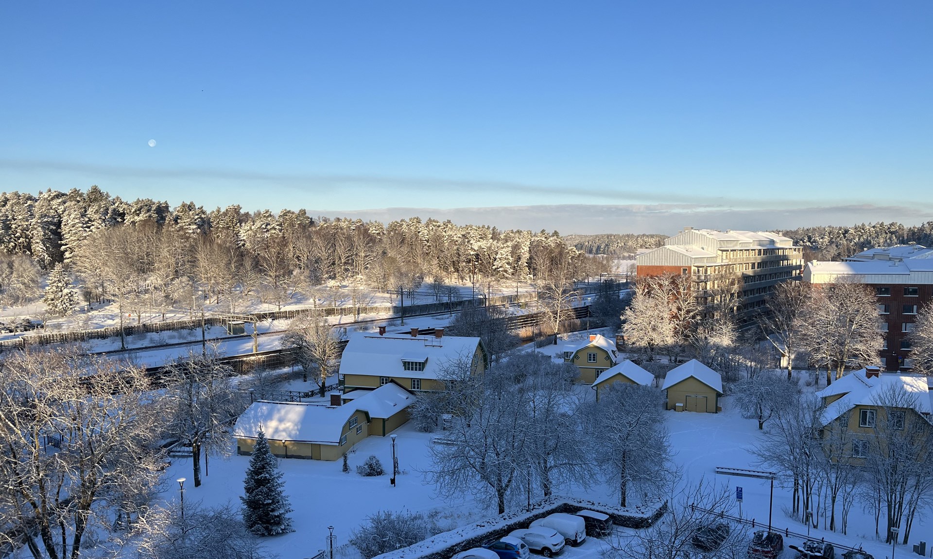 Vinterlandskap med trähus i gult och grönt och en järnväg i bakgrunden.