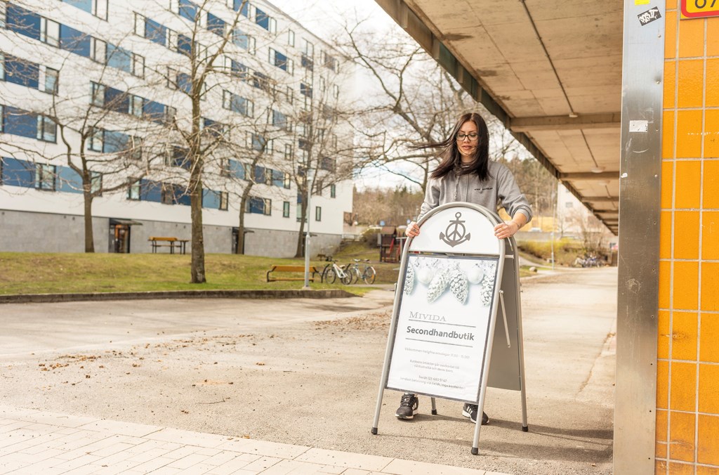 Kvinna vid en skylt på en gård med ett flerfamiljshus i vitt i bakgrunden