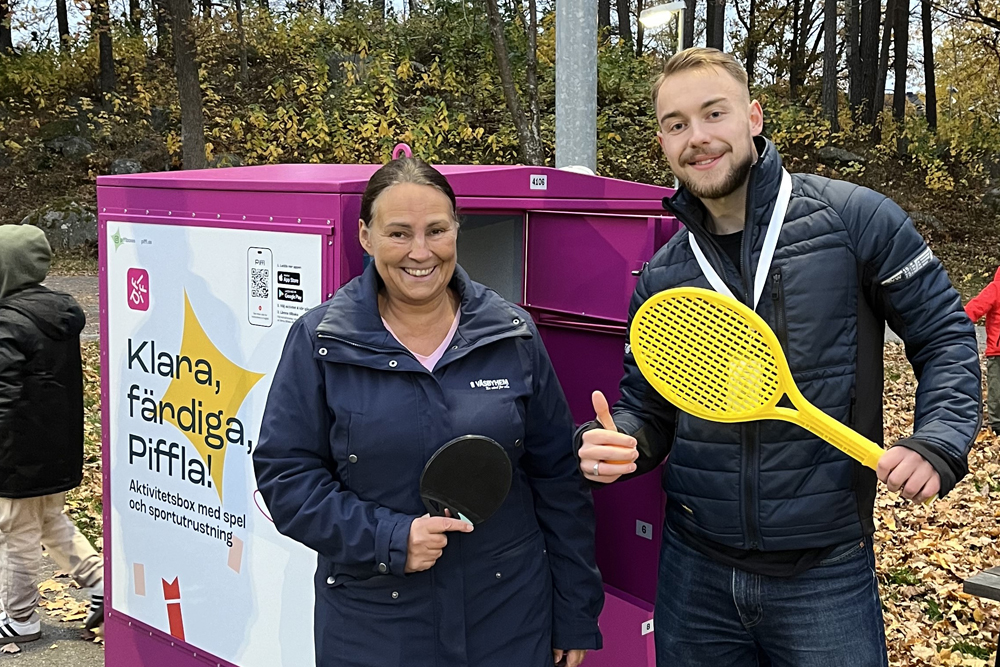 En kvinna och en man med gult racket står framför en lila aktivitetsbox.