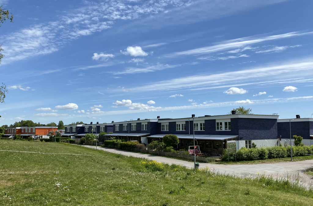 Radhus i lila tegel och orange tegel med uteplatser och en gräsmatta och gångväg i förgrunden