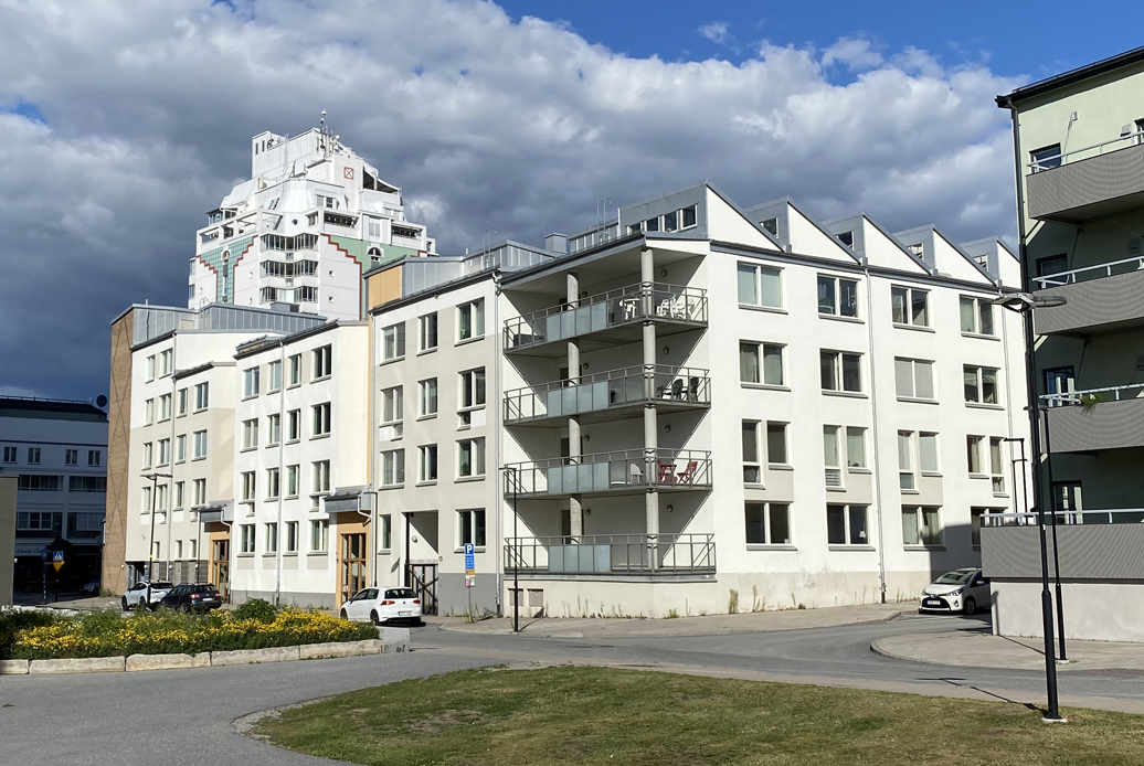 Flerbostadshus i vitt med gång- och gatuväg i förgrunden