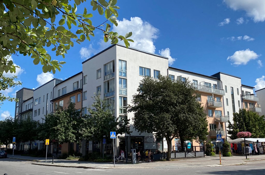 Gatuvy med trafikskyltar, träd och flerbostadshus i vitt, grått och beige