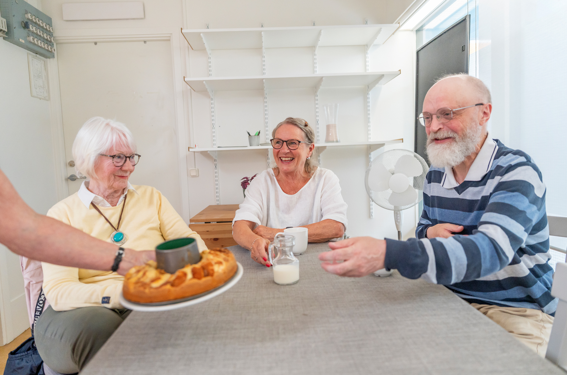 Två kvinnor och en man sitter kring ett fikabord.